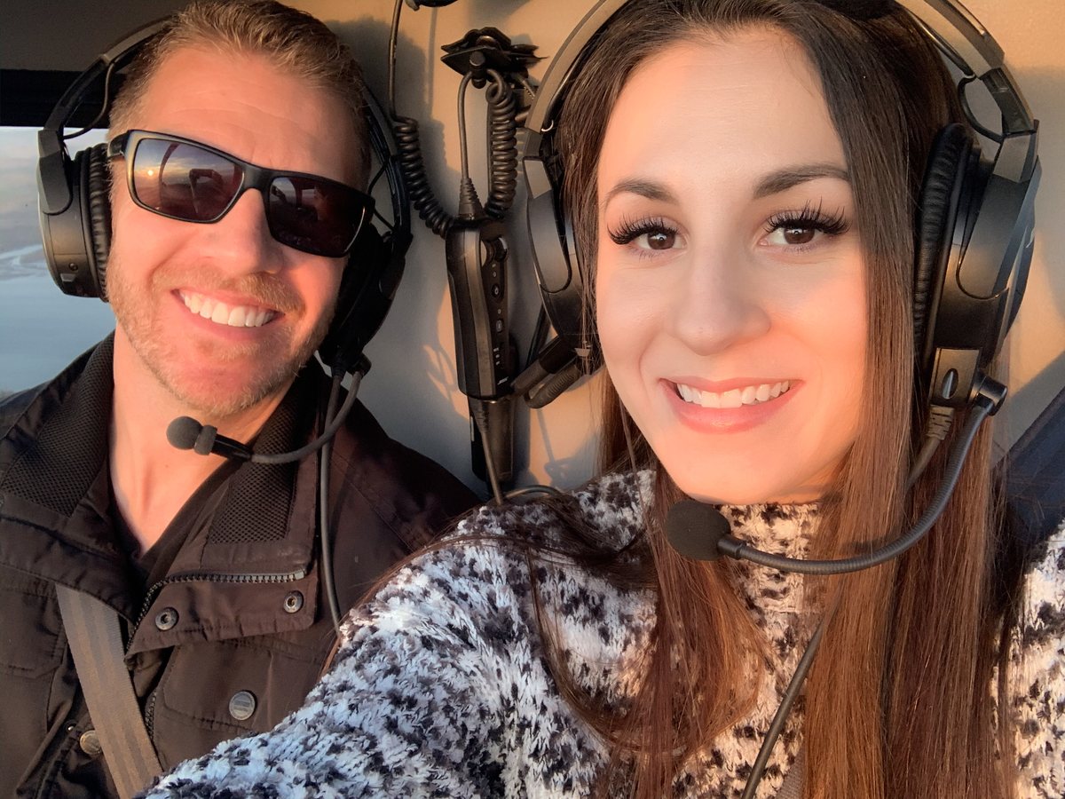 Adam and Micaela in the cockpit of a light aircraft, both
                  wearing headsets.