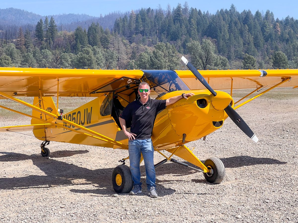 Adam beside a yellow tailwheel aeroplane on a
                                   gravel strip.